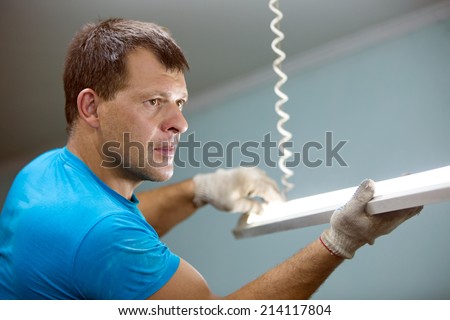 Electrician man worker installing ceiling fluorescent lamp