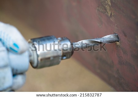 Worker drilling metal sheet closeup with hand drill