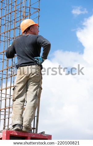 Builder man worker mounting concrete formwork during construction works at blue sky clouds background