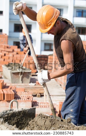Construction manual bricklayer worker mixing concrete adhesive mixture with shovel during masonry works