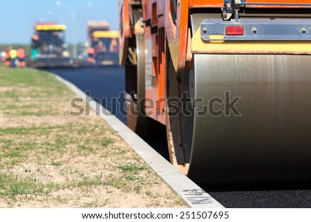 Road roller compacting asphalt  near curb stone