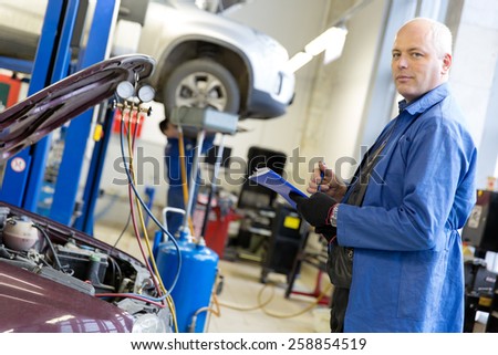 Caucasian mechanic engineer with notebook during car air conditioner refilling on automobile service station background