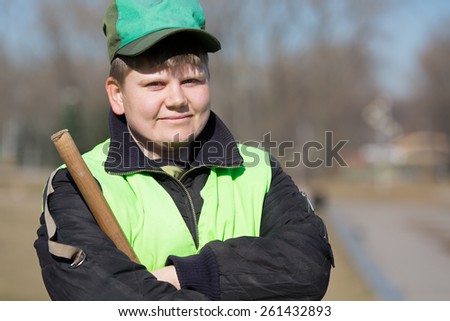 Portrait of positive smiling street sweeper in city park with broom tool and crossed arms\
,