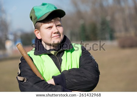 Portrait of positive smiling street sweeper in city park with broom tool and crossed arms\
,