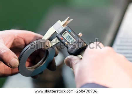 Factory man worker measuring steel detail with digital Vernier Caliper at workshop