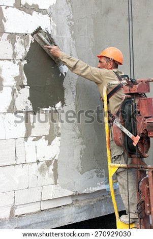 Plasterer crafts man builder worker plastering multi storey building wall of bricks or concrete blocks during finishing construction works