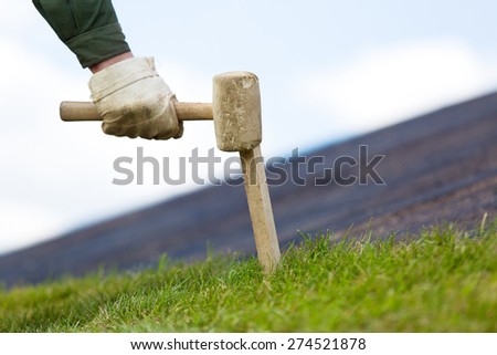 landscaper worker fixing rolled sod grass turf on soil for new lawn with wood stick and hammer tool