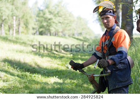 Portrait landscaper man worker during grass cutting with gas handheld string trimmer equipment
