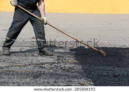 Road worker leveling fresh asphalt during asphalt pavement repair or construction works