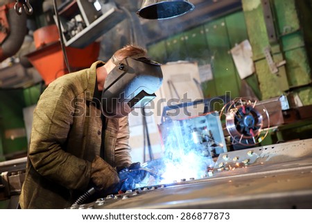 Manufacture worker welding metal at factory workshop with flying sparks