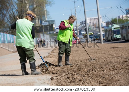 City landscapers female workers preparing soil along street for grass planting with rake tools
