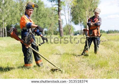 Positive landscapers men workers with gas handheld string trimmers equipment during grass cutting team works