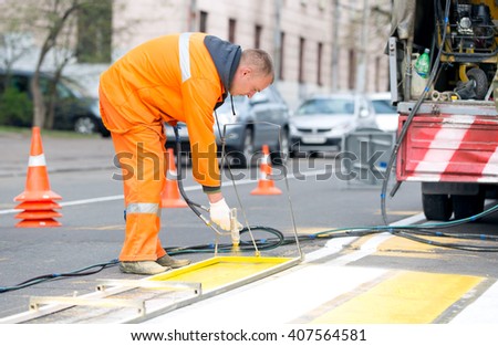 Technical road man worker painting and remarking pedestrian crossing lines on asphalt surface using paint sprayer gun during capital street pavement maintenance works