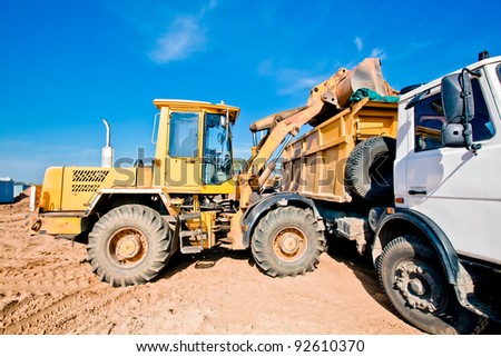 Wheel loader machine loading into dumper truck tipper soil at construction site