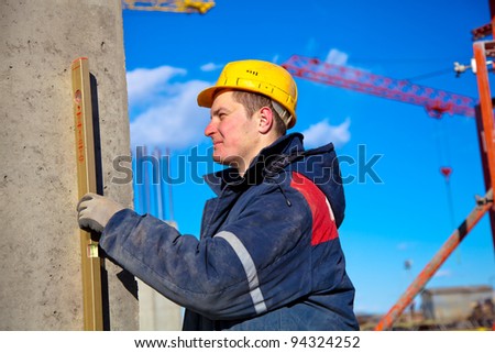 Builder worker with hardhat using water level at construction site during checking vertical level of house wall