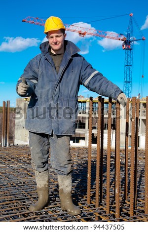 Smiling builder worker standing at construction site on rebar during concrete pouring works and showing a thumb up