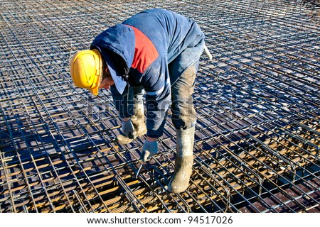 Builder worker in hardhat and uniform installing binding wires to reinforcement steel bars at construction site
