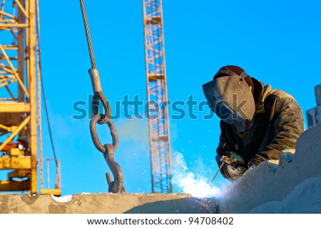 Builder worker welder during installation of house wall panels using blind welding machine and tower crane
