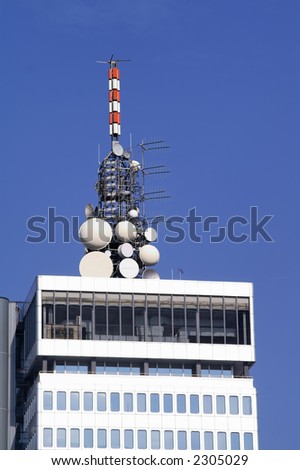 Cluster of different microwave antennae on top of a high rise modern office building