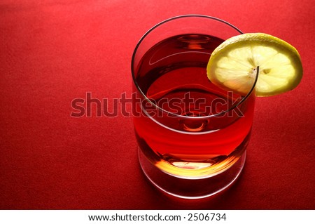Glass of red liquid (wine,  tea, etc.) with lemon slice (horizontal) in red background