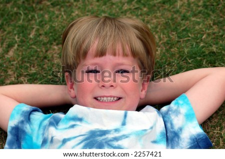 Smiling six year old boy lying down on his back in the grass.