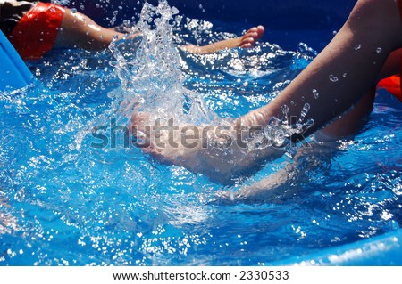 Two boys kicking in a kiddie pool.
