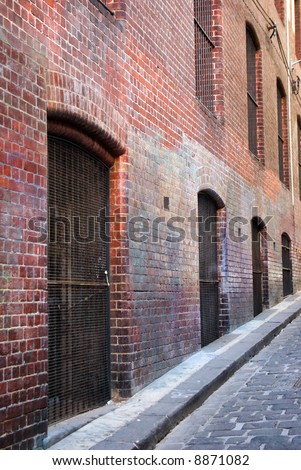 Grunge image of cobbled urban lane with red brick wall