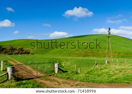 Green farmland with windmill and farm gate in foreground