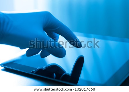 Hand in blue glove touching modern digital tablet. Concept image on medical or research theme.