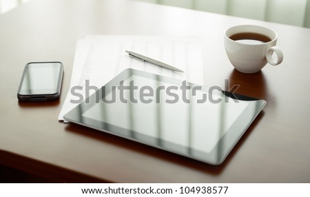 Modern workplace with digital tablet computer and mobile phone, cup of tea, pen and paper with numbers.