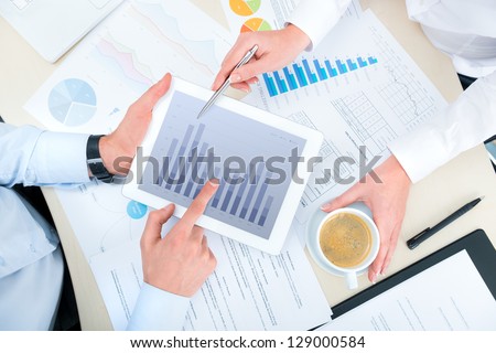 Business people discussing and analyzing market data information on a modern digital tablet computer. Top view photoshoot.
