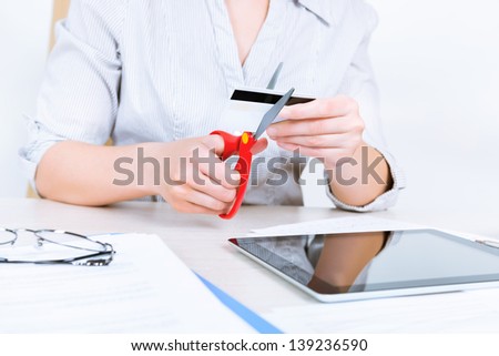 Businesswoman sitting at desk in the office and getting rid of her credit card with the help of scissors after paying back a loan
