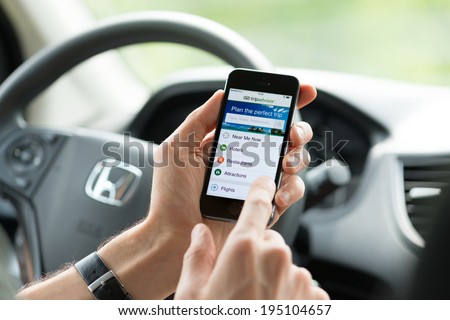 KIEV, UKRAINE - MAY 16, 2014: Man in a car planning a trip using Tripadvisor app on Apple iPhone 5S. Tripadvisor is a travel guide source providing reviews, photos and advice for hotels and vacations.
