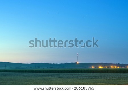 Distant vineyard hills and agricultural corn field with village lights at summer night