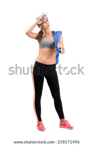 Young tired fitness woman wiping sweat from forehead with cool water bottle. Full body length portrait isolated over white background.