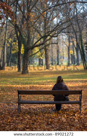 Alone woman or girl sitting in the autumn park waiting for someone.