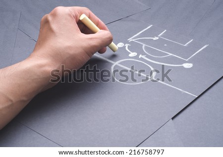 Hand drawing the attacking strategy for football game with chalk on the black project paper