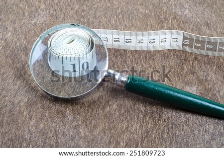 Magnifying glass focusing at numbers on measurement tape over the sparkling brown background