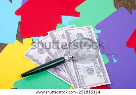 Magnifying glass focused at the money over the colorful house paper cut-out