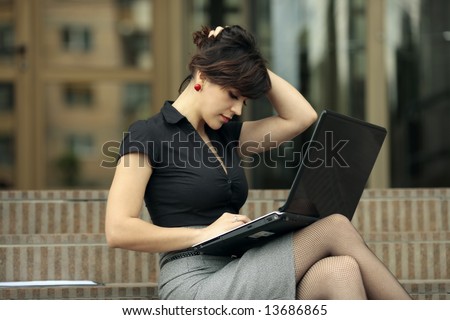 Busy lady with sexy legs. Young attractive business lady working at the laptop outdoors and playing with her hair