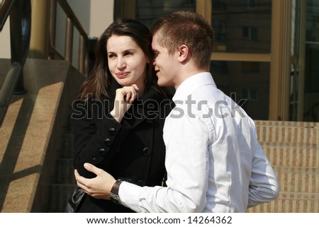 young couple outdoors holding and man whispering something in the young attractive lady\'s ear