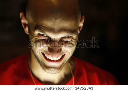 Terrifying terrorist. A scary man looking at the camera with face lighted from under his chin and with a grin as a smile. Look into my portfolio for a not smiling version