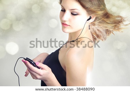 Attractive teen age girl listening to music with mp3 player and earphone with hair blowing in the wind on bokeh background