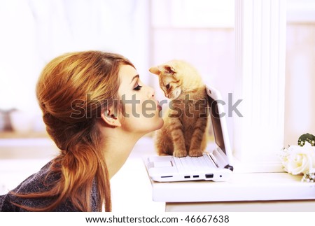 Gorgeous blond fashion model kissing a little cat\'s nose staying on a laptop notebook inside a beautiful home in the chicken