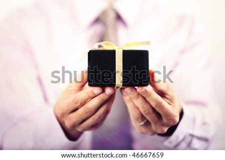 Business man in suit offering gift box straight to the camera