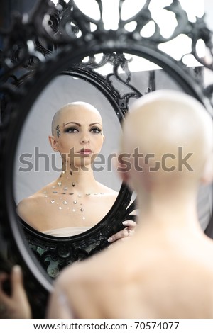 Real bald cancer survivor woman looking calmly into the mirror