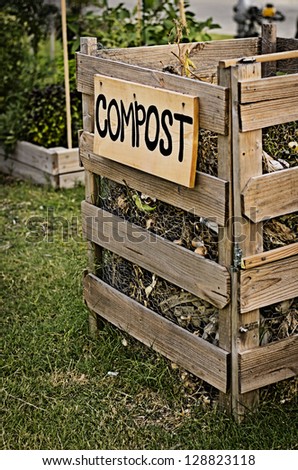 Compost bin in the grass next to a community vegetable garden.