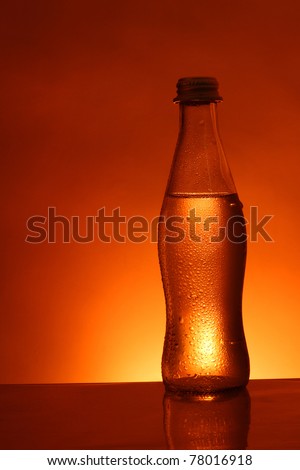 Water-filled glass bottle with water droplets on surface in red background