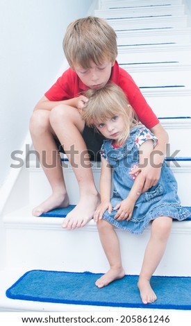 A sad brother and sister sitting on the stairs of the family home.