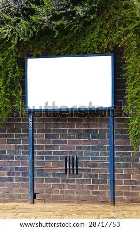 Blank sign surrounded by textured brick wall and green foliage.
